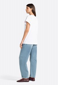 Weißes T-Shirt mit kurzen Ärmeln und lockerer Passform, kombiniert mit hellblauen, weit geschnittenen Jeans und burgunderfarbenen Schnürschuhen. Glatte Textur.