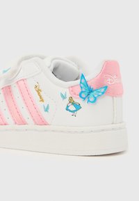 Biele a ružové detské tenisky s motívom Disney Alice v krajine zázrakov a modrým motýľom zdobené na päte a boku.