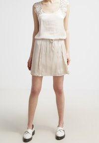 Robe couleur crème avec bordure en dentelle sur les bretelles, taille ajustable par cordon, et tissu doux et fluide. Associée à des chaussures blanches sans lacets.