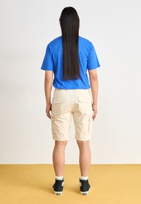 Chemise bleue à manches courtes, short cargo beige avec poches, et baskets montantes noires avec accents blancs, vues de l'arrière.