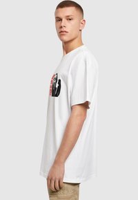 Hvid bomulds-T-shirt med korte ærmer, prydet med et grafisk tryk i rød og sort, der viser et spøgelsesansigt og tekst på fronten.