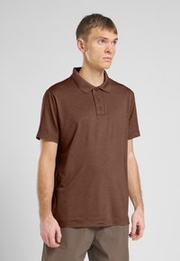 Polo marron à manches courtes, col classique, patte de boutonnage à trois boutons et tissu texturé. Porté avec un pantalon marron clair.
