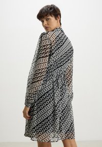 Abito nero e bianco trasparente con motivo a catena, maniche lunghe e vita arricciata, caratterizzato da un design fluido e una texture morbida.