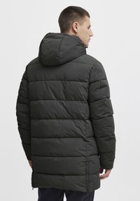 Padded parka u tamnozelenoj boji, s kapuljačom, kanalom zapakiranim dizajnom i patentnim zatvaračima sa strane za poboljšanu mobilnost.