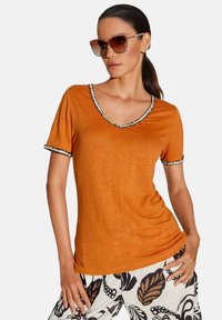 Oranje V-hals T-shirt met korte mouwen, zwart-wit afgewerkte halslijn, zacht materiaal, gecombineerd met gestreepte broek.