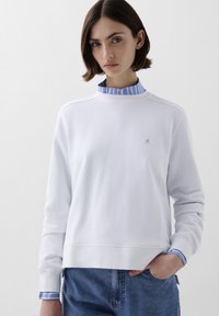 Hvid sweatshirt lavet af tekstureret stof, med rund hals og blåstribede skjortemanchetter. Lille logo detalje på brystet.