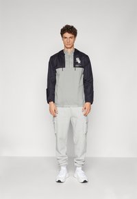 Lightweight windbreaker with a black top half and gray bottom, featuring a front logo, paired with light gray cargo sweatpants and white sneakers.