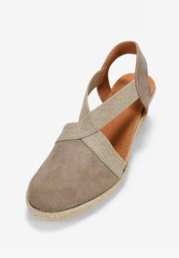 Sandalia de esparto beige con tiras cruzadas, parte superior de ante y suela de yute trenzado. Interior acolchado y detalles elásticos para mayor comodidad.