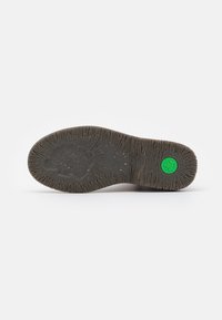Suela de zapato de goma marrón con estrías texturizadas, con un logo circular verde en el lateral. La superficie está ligeramente desgastada y es desigual.