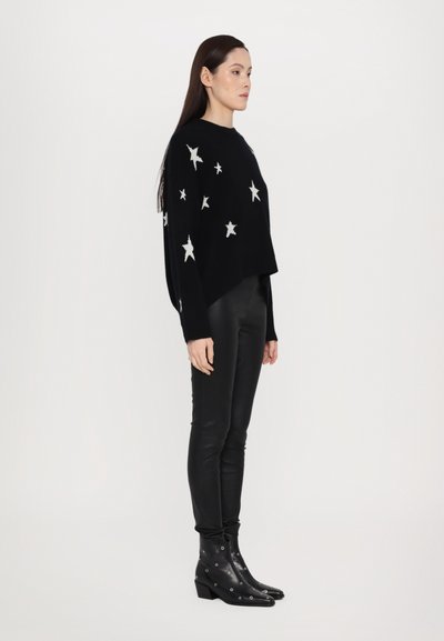 Black knitted sweater with white star patterns, cropped design, paired with black fitted pants and ankle boots featuring silver grommets.