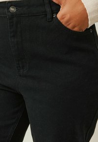 Pantaloni in denim nero con una texture liscia, dotati di tasca frontale e dettaglio in metallo sul punto vita, design aderente.
