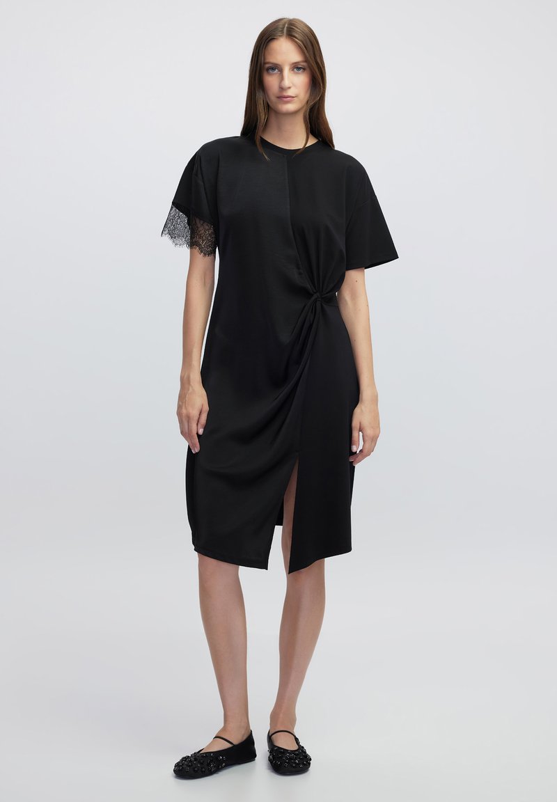 Robe noire avec un détail avant torsadé, coupe jusqu'au genou, manches courtes avec des accents en dentelle et une légère fente sur le côté.
