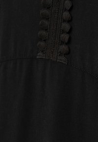 Musta vaate, jossa on teksturoitu nauha pyöreillä kangaspainoituksilla vetoketjun varrella, esittelee sileää kangasta, jossa on hieno kiilto.