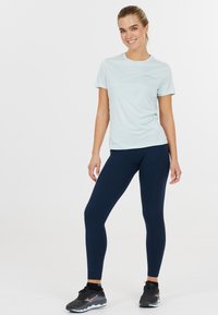 Vaaleansininen urheilupaita, jossa on lyhyet hihat, yhdistettynä tummansinihin legginsseihin, joissa on hienovarainen ommeltu kuvio, sekä mustiin urheilukenkiin.