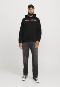 Sort hætte sweatshirt med "JACK & JONES" logo, frontlomme, parret med slidte grå jeans og sorte sneakers med hvide såler.
