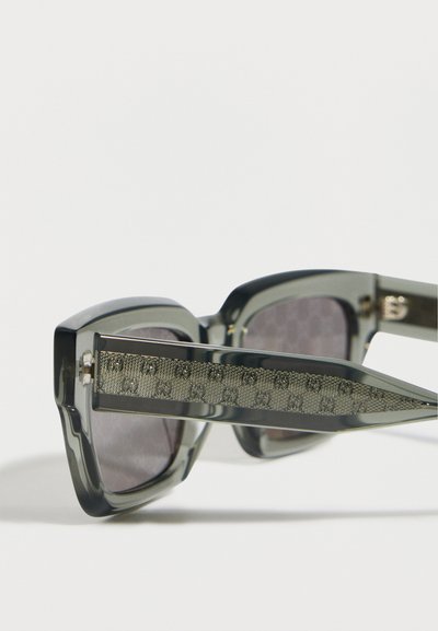 Γκρι διαφανή γυαλιά ηλίου με τετράγωνα πλαίσια και βραχίονες που διαθέτουν μεταλλική επένδυση με μοτίβο και διπλά λογότυπα G.