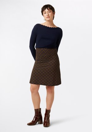 Marineblauer, gewellter Pullover, gemusterter dunkler Rock mit gelben und roten Akzenten, kombiniert mit glänzenden burgunderfarbenen Knöchel-Stiefeln, die ein lässiges Outfit bilden.