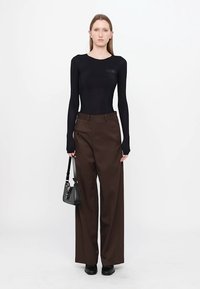Black long-sleeve top paired with brown wide-leg trousers and black shoes. Small shoulder bag slung in hand. Simple, modern design.