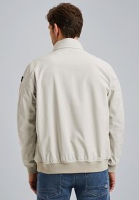 Light beige bomber jacket with a ribbed hem and cuffs, featuring a back yoke and subtle stitching details. Smooth texture, minimal design.