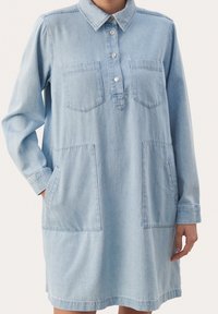 Abito in denim azzurro chiaro con maniche lunghe, colletto con bottoni, due tasche frontali e vestibilità morbida. Texture liscia, design casual.