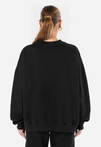 Fekete, oversize pulóver kerek nyakkal, ejtett vállakkal és bordás mandzsettákkal, puha, tartós anyagból készült.