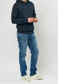 Sudadera con capucha azul marino con un logotipo en la parte frontal, combinada con jeans de mezclilla azul claro y zapatillas de deporte color crema. Tejido suave, corte casual.
