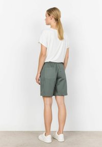 Groene shorts met elastische taille en twee achterzakken, gecombineerd met een wit shirt met korte mouwen. Model is van achteren afgebeeld. Sneakers inbegrepen.
