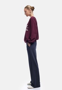 Burgundy oversized sweatshirt med vit text, tillsammans med marinblå sweatpants. Har en avslappnad passform och sidofickor. Vita sneakers.