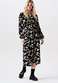 Zwart en beige maxi-jurk met bloemenpatroon, lange mouwen, verzamelde taille en een ontspannen pasvorm. Gepaard met chunky zwarte schoenen en sokken.