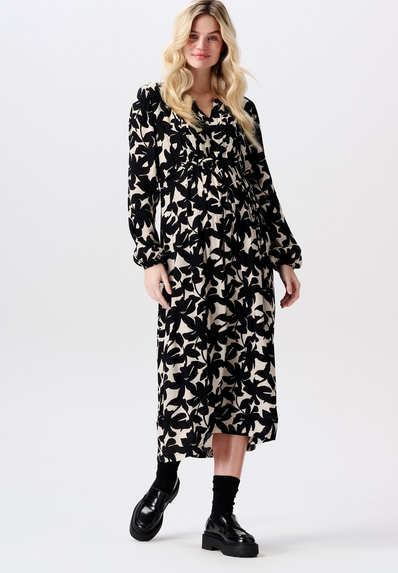 Zwart en beige maxi-jurk met bloemenpatroon, lange mouwen, verzamelde taille en een ontspannen pasvorm. Gepaard met chunky zwarte schoenen en sokken.