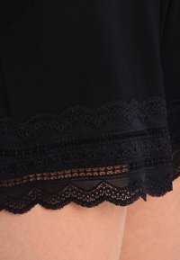 Shorts en tissu noir avec un ourlet en dentelle festonnée. Présentent des motifs de dentelle élaborés et une texture douce, créant un contraste sur le bord inférieur.
