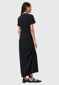 Abito maxi nero con maniche corte, caratterizzato da un dettaglio drappeggiato laterale e una silhouette fluida. Tessuto liscio con una leggera lucentezza.