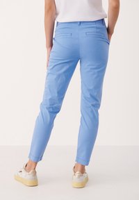 Pantalon bleu clair sur mesure en coton, avec une coupe slim, deux poches arrière et des revers roulés, associé à des baskets blanches.