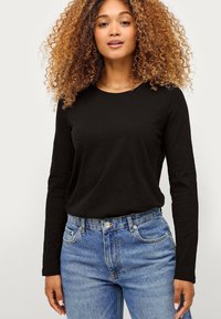 Zwarte lange mouwen t-shirt met een ronde hals, gecombineerd met lichtblauwe high-waisted denim jeans met voorzakken en een knoopsluiting.