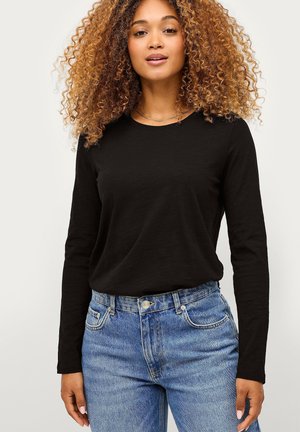 Zwarte lange mouwen t-shirt met een ronde hals, gecombineerd met lichtblauwe high-waisted denim jeans met voorzakken en een knoopsluiting.