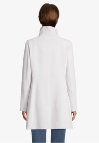 Abrigo blanco con cuello alto, mangas largas y silueta en A. Textura suave y diseño minimalista sin hardware visible.