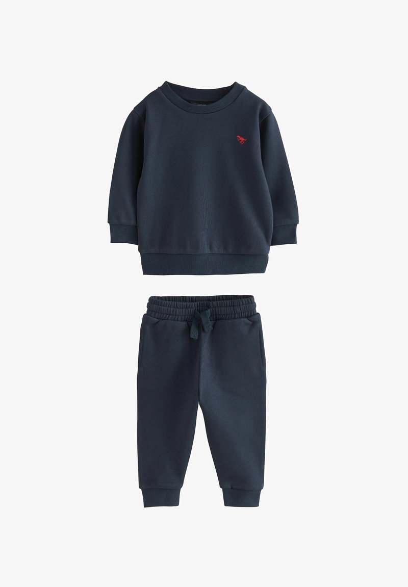Felpa blu navy con polsini a coste e colletto tondo, caratterizzata da un piccolo logo rosso. Pantaloni coordinati con vita elasticizzata e gamba affusolata.