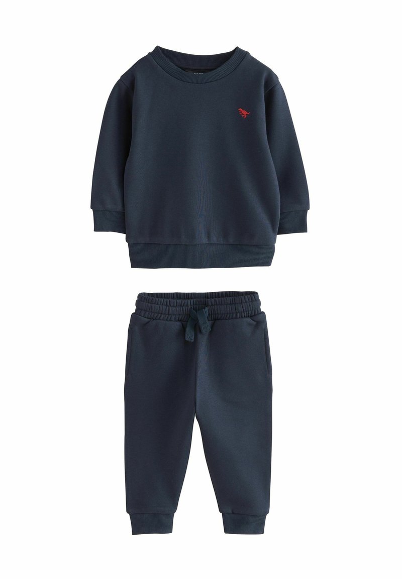 Sweat-shirt bleu marine avec des poignets et un ourlet côtelés, arborant un petit logo rouge brodé. Pantalon de survêtement assorti avec une taille élastique et des jambes fuselées.