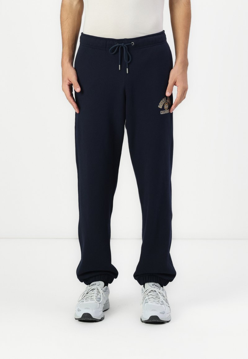Marineblå joggebukser med elastisk midje, snøring og tapered mansjetter. Har en frontlogo i lyse farger.