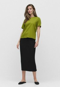 Grön kortärmad t-shirt kombinerad med en svart ribbad midi-kjol, kompletterad med svarta slipskor. Enkelt mönster och jämn textur.