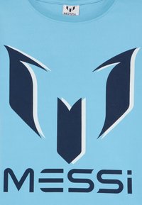 Šviesiai mėlynas medvilnės marškinėliai su tamsiai mėlynu grafiniu dizainu, turinčiu aštrias formas ir žodį "MESSI" ryškiomis raidėmis apačioje.