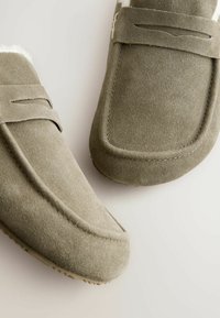 Chaussons en suède gris à enfiler avec une douce doublure en shearling, présentant un design cousu et une semelle en caoutchouc pour une traction et un confort optimaux.