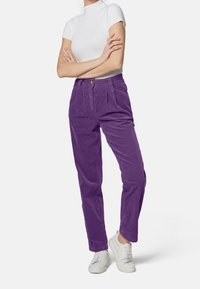 Pantaloni a coste viola con vita alta, pieghe frontali e tasche laterali, abbinati a una maglietta bianca aderente e sneakers bianche.