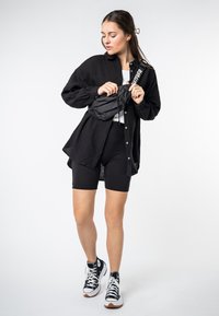 Oversized black button-up shirt, white cropped top, black biker shorts, black fanny pack with white strap, and black high-top sneakers.