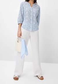 Blouse à manches longues bleu clair avec motif géométrique, associée à un pantalon en lin blanc et un sac à main crème avec une écharpe à rayures bleu clair.
