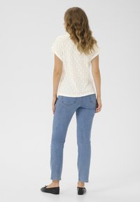 Hvid strikket top med diamantmønster, kombineret med lyseblå skinny jeans og sorte slip-on sko. Set fra ryggen.
