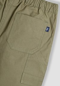 Pantalons cargo verts avec une taille élastique, dotés d'une grande poche latérale et d'une petite étiquette de marque bleue sur le côté. Tissu texturé.