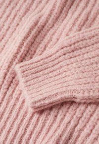 Rosa gestrickter Pulloverstoff mit einer gerippten Struktur und einem umgeschlagenen Bündchen. Das Garn wirkt weich und flauschig und betont das grob gestrickte Design.