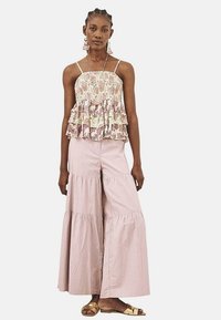 Top de tirantes en capas con estampado floral en tonos pastel, combinado con pantalones de campana en rosa claro y sandalias planas doradas.