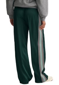 Grüne Satin-Hosen mit lockerer Passform, die vertikale Streifen in Weiß, Rot und Hellblau an den Seiten sowie einen elastischen Bund aufweisen.